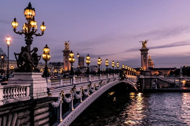 Pont Alexandre III bridge in Paris lit up at dusk, with golden statues and lamps reflecting on the Seine River